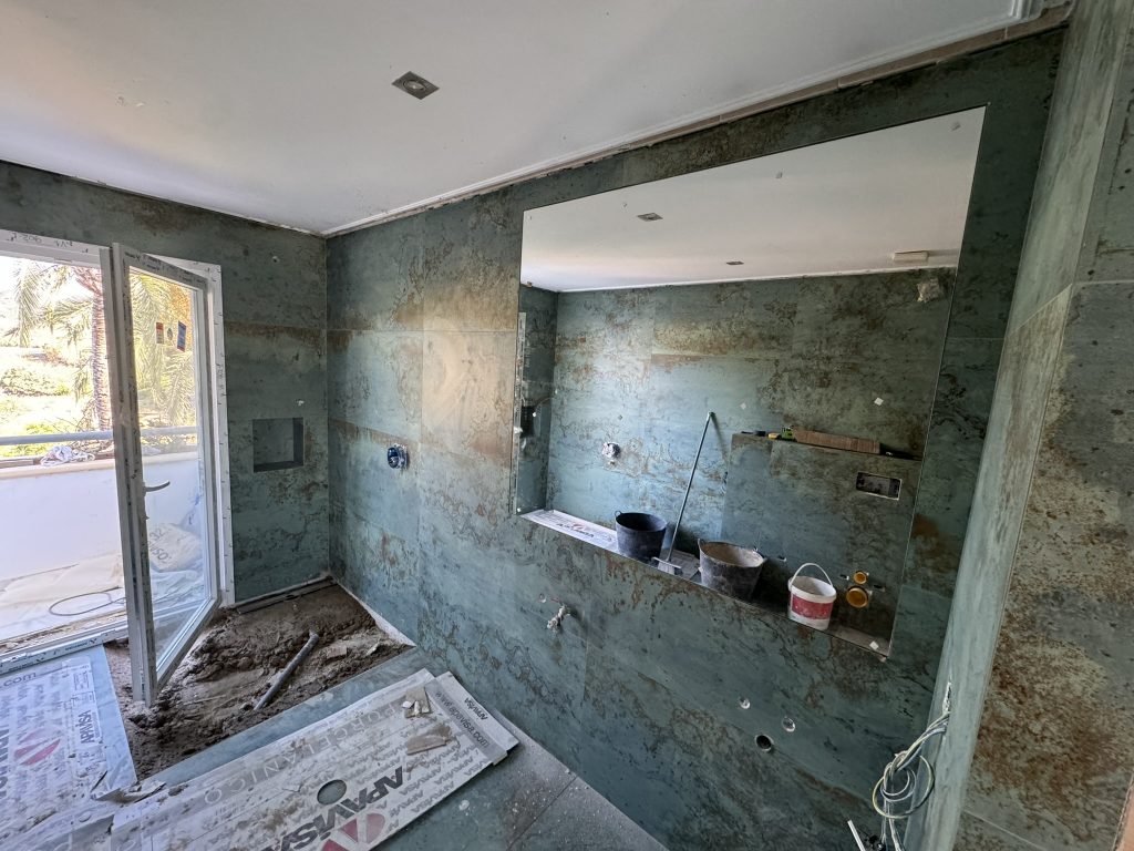 Baño en proceso de reforma con revestimiento en piedra verde y espejo grande
