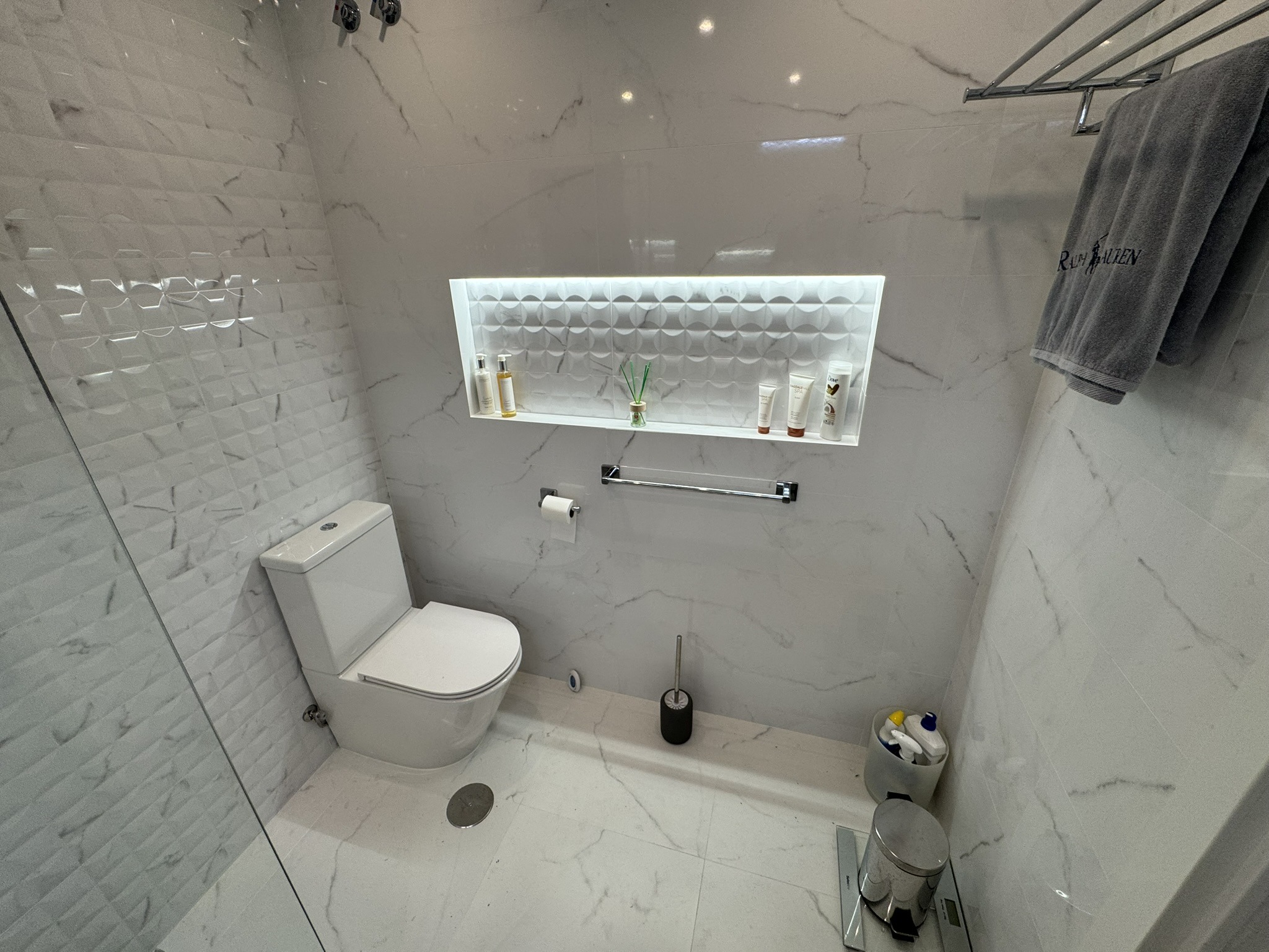 Baño moderno con revestimiento de mármol blanco, hornacina iluminada y azulejos en relieve