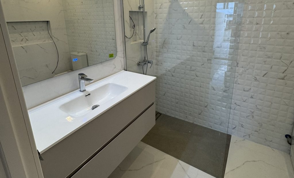 Baño moderno con lavabo blanco y ducha tipo walk-in con mampara de vidrio