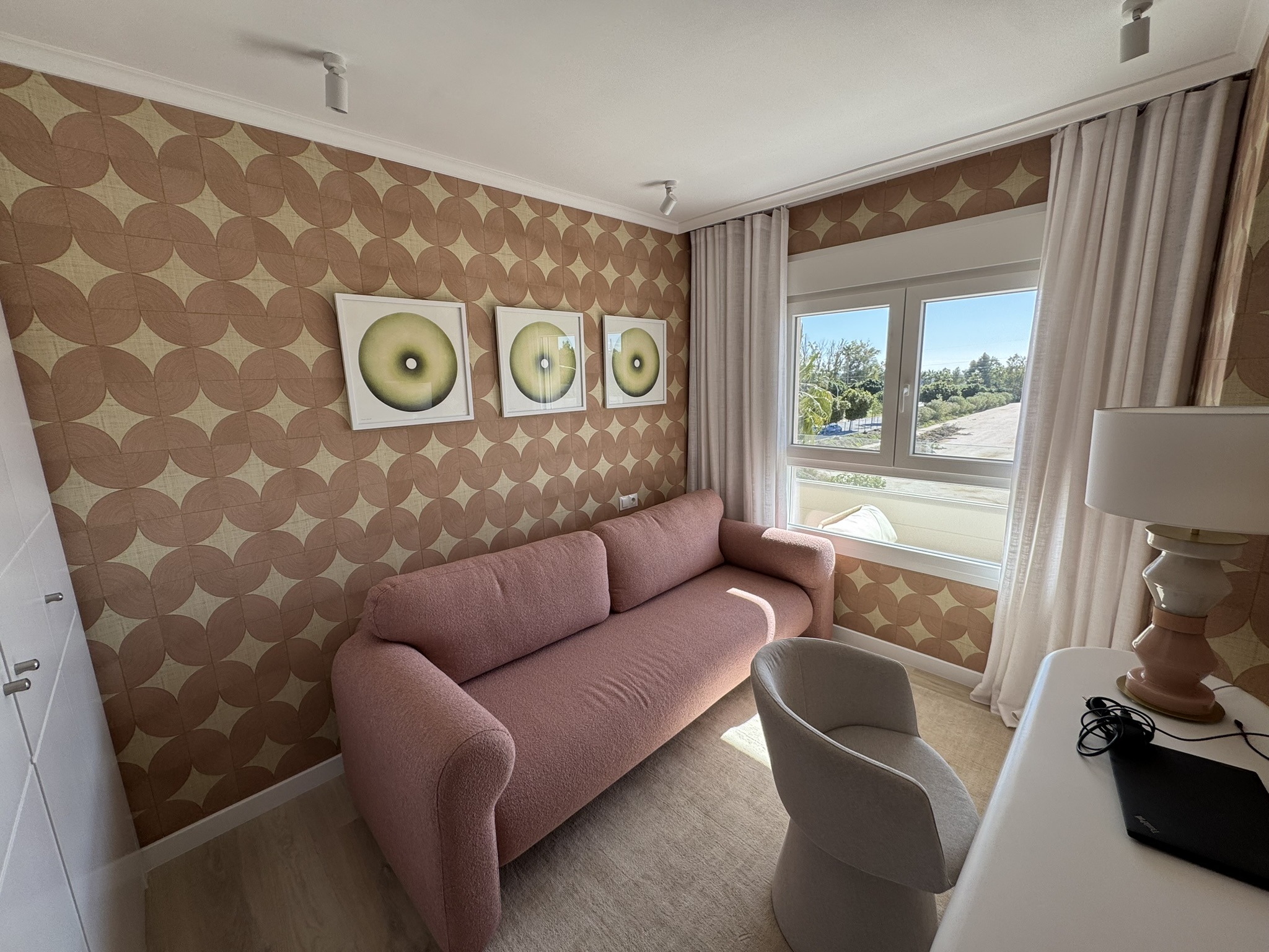 Sala pequeña con sofá rosa, escritorio blanco y papel pintado geométrico retro