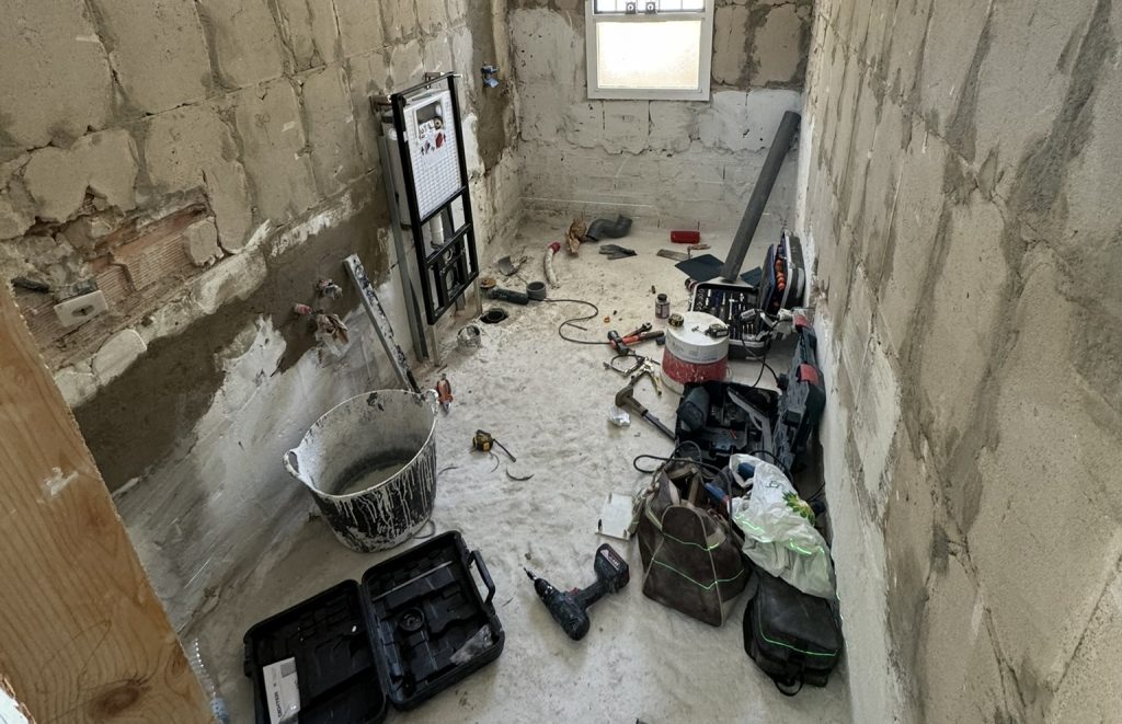Baño en reforma con instalaciones expuestas y herramientas de obra