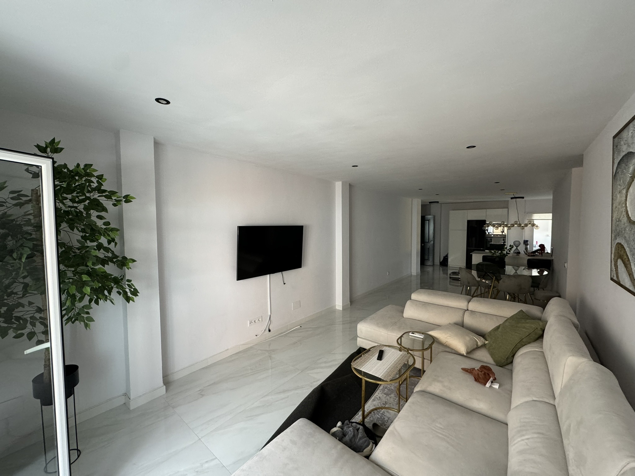 Sala de estar contemporánea con sofá esquinero, planta decorativa y lámpara de araña