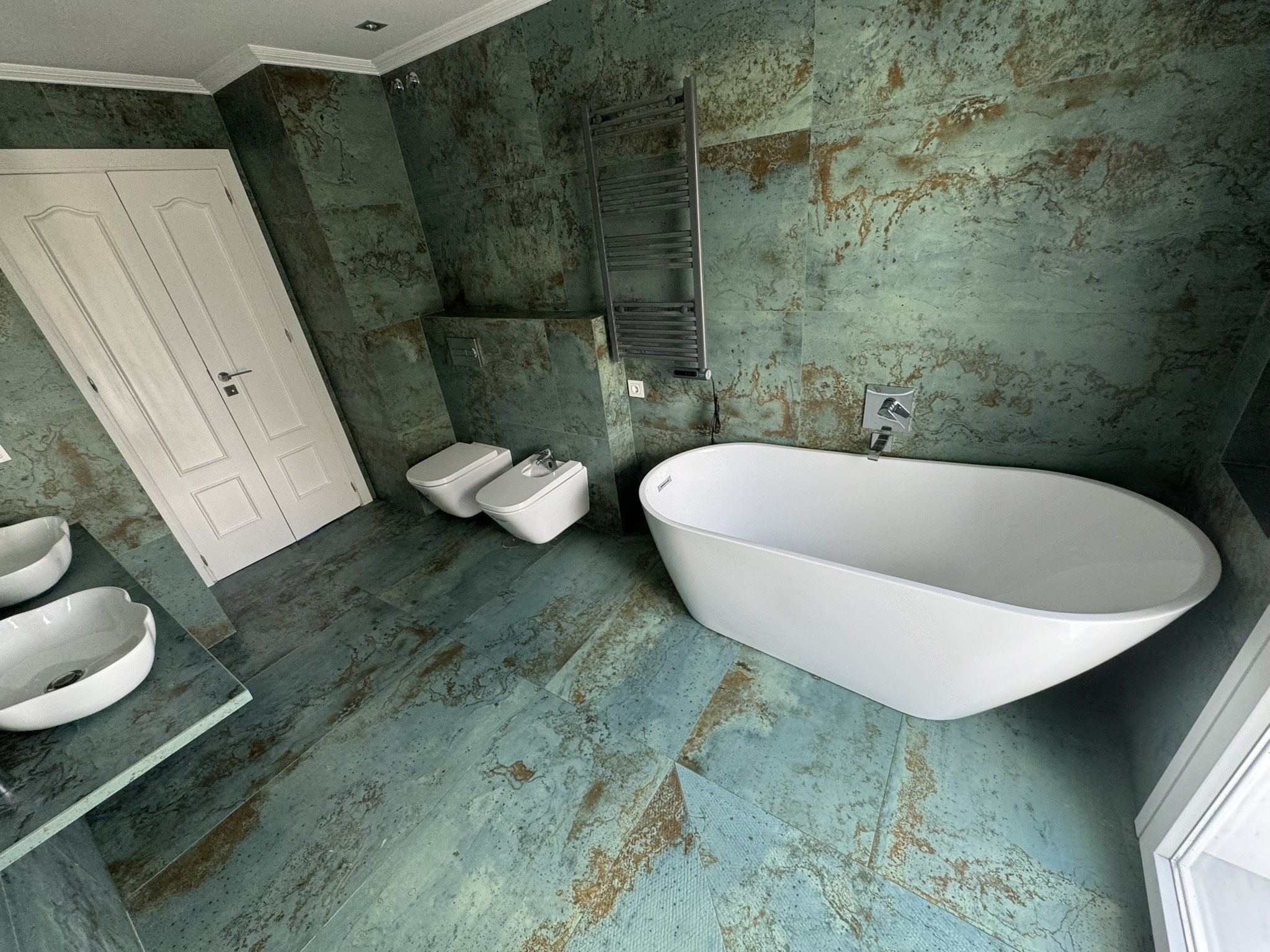 Baño moderno con revestimiento verde oxidado y bañera exenta blanca