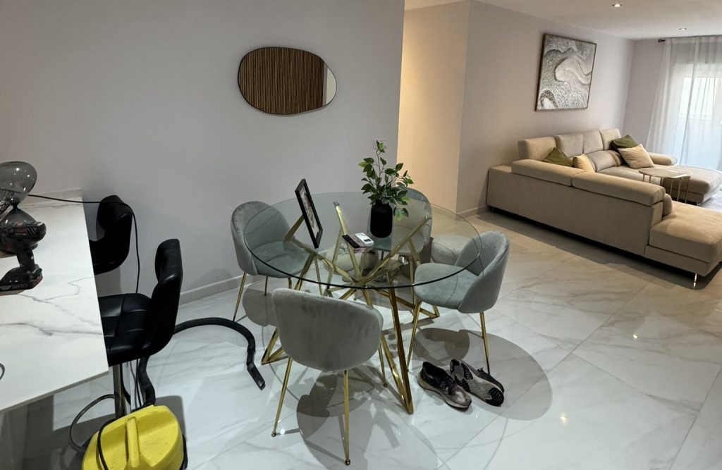 Comedor moderno con mesa de cristal y salón integrado con sofá beige y suelo de mármol