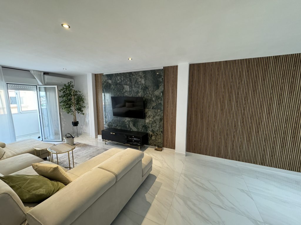 Sala de estar minimalista con sofá beige y televisor en pared de piedra natural